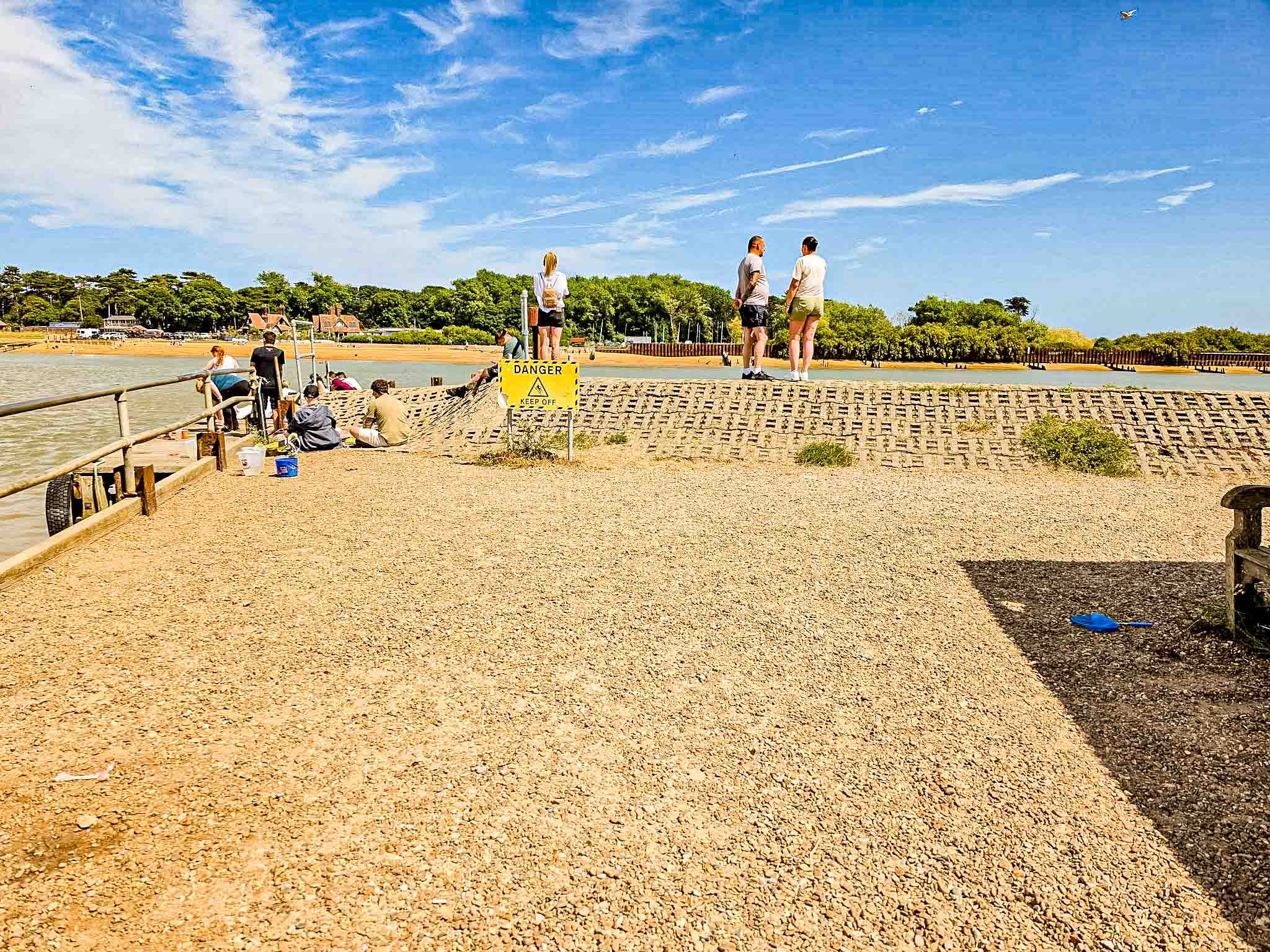 Beach 26 — people on the shingle below a Danger Keep Off sign